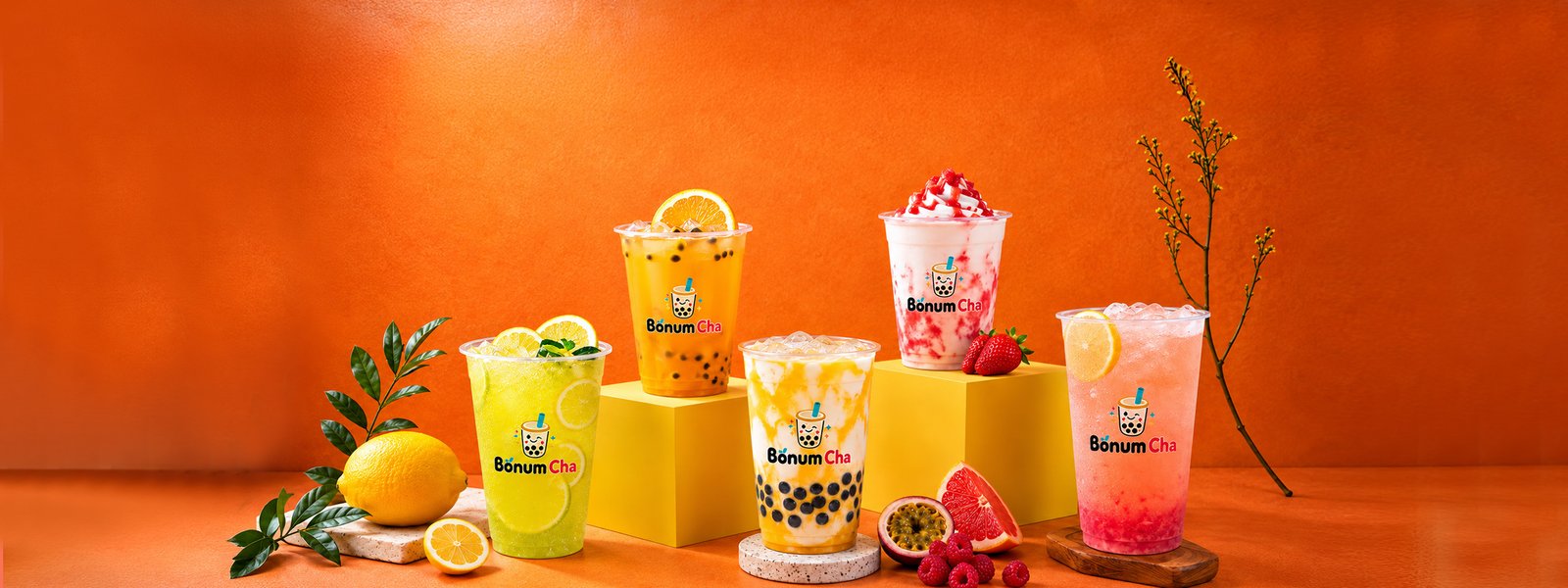 Bōnum Cha bubble tea, fruit tea and ice cream tea cups displayed on yellow podiums with fresh lemon, passion fruit, grapefruit, strawberries and raspberries